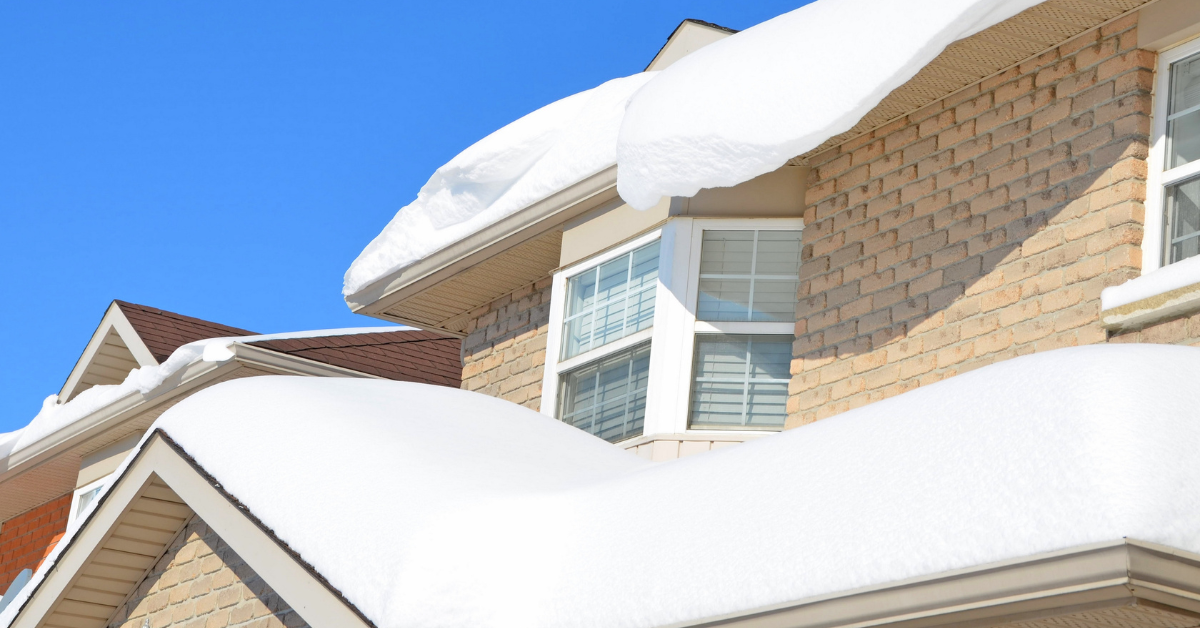 snow covering roof of a tan brick house