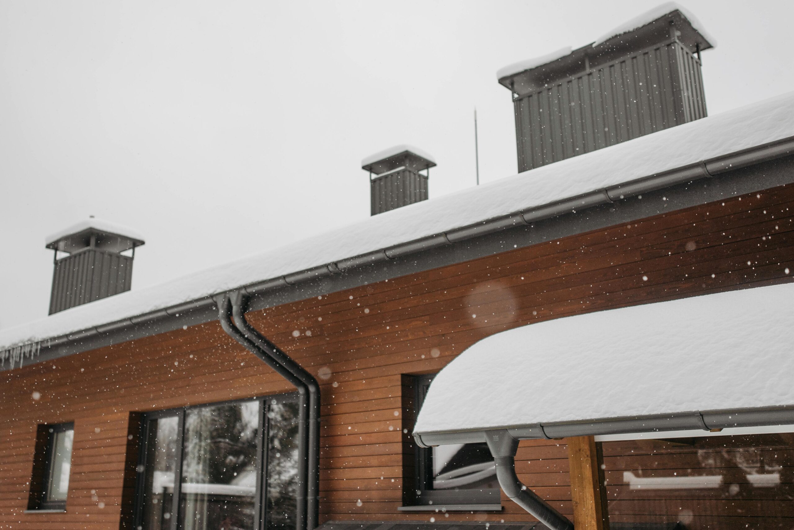 Snow covers the roof of a wood paneled house in the winter.