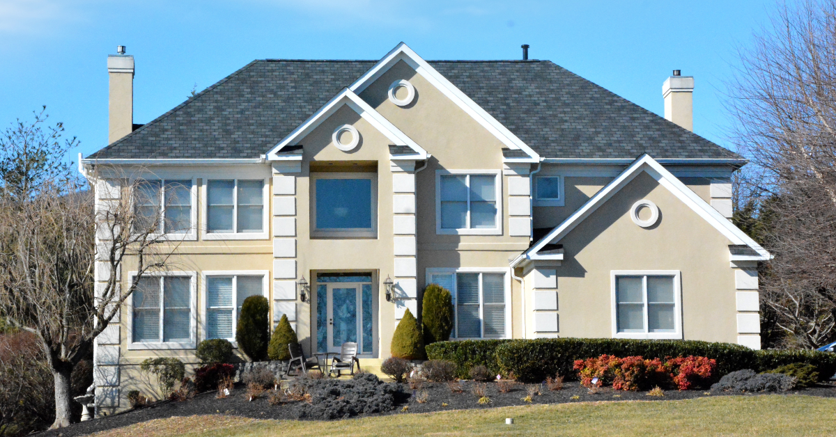 Standing out in front of an elegant, large home featuring immaculate landscaping.