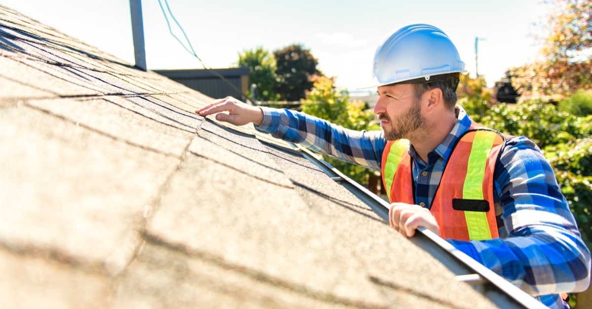A roofing contractor inspecting shingles for signs of wear during a routine roof maintenance visit.